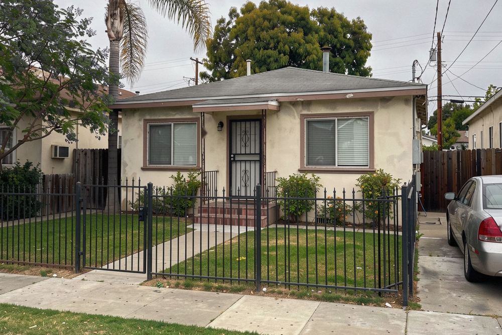 Small stucco bungalow behind a wrought-iron fence