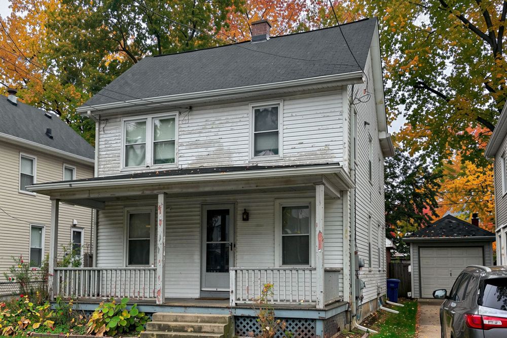 Older two-story frame house with a covered front porch and fall leaves